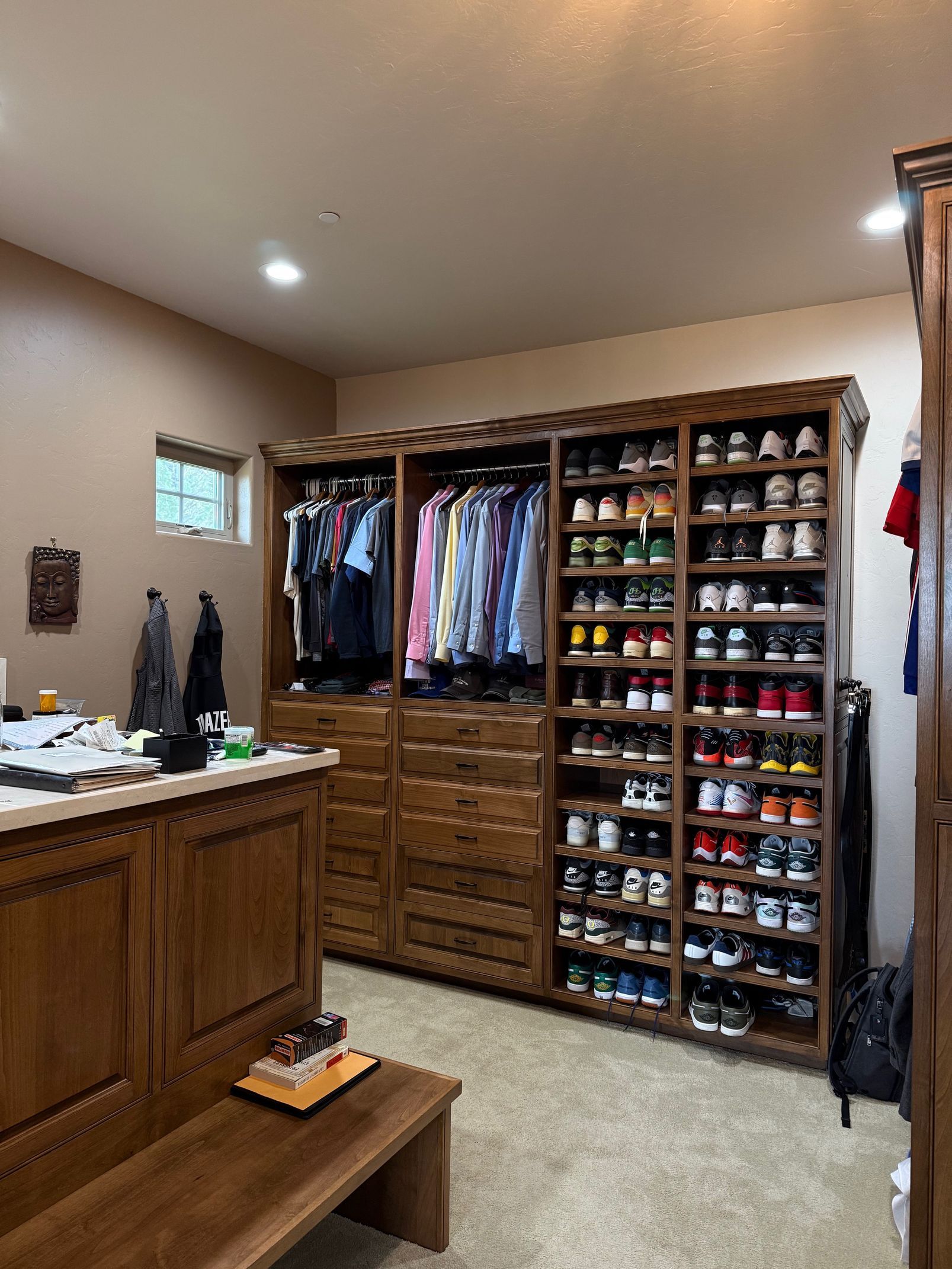 Walk-in closet with clothes, shoes, and drawers, plus a bench and vanity in a carpeted room.