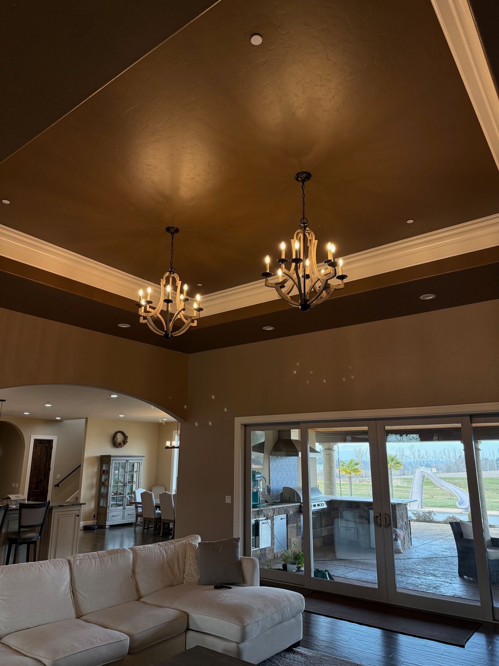 Elegant living room with beige sectional, chandeliers, and large glass doors opening to a bright patio.