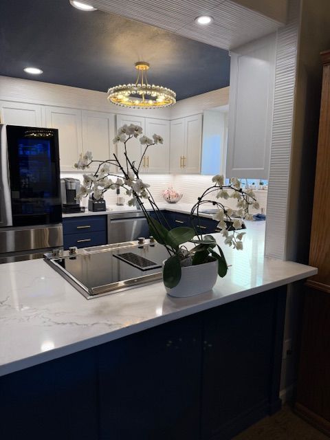 Modern kitchen with dark cabinets, white marble island, and orchid centerpiece under a chandelier.