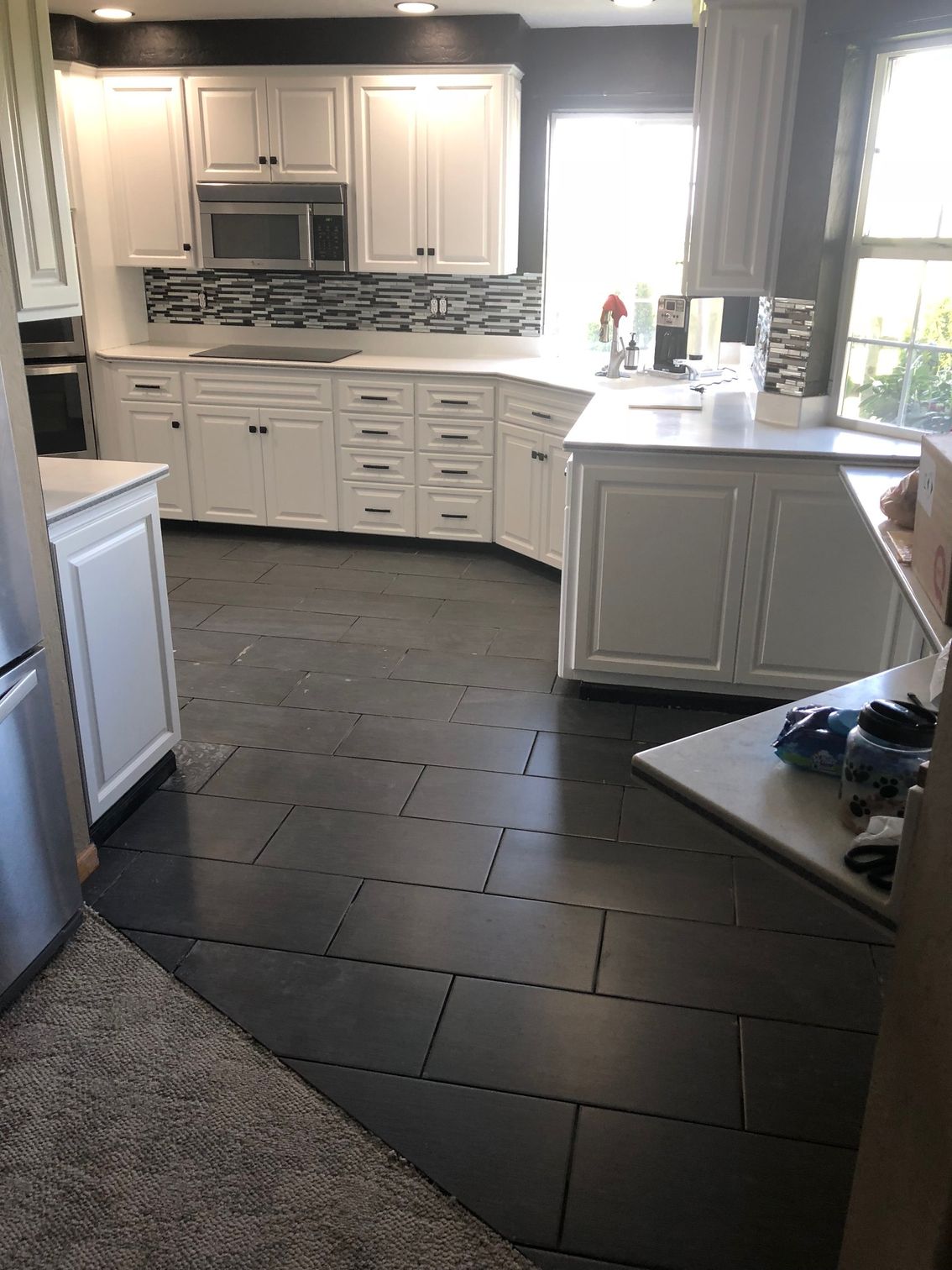 Bright kitchen with white cabinets, dark floor tiles, and sunlight from a window