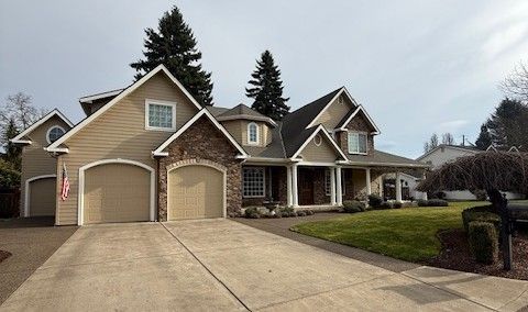 Suburban two-story house with tan siding, double garage, and a wide concrete driveway