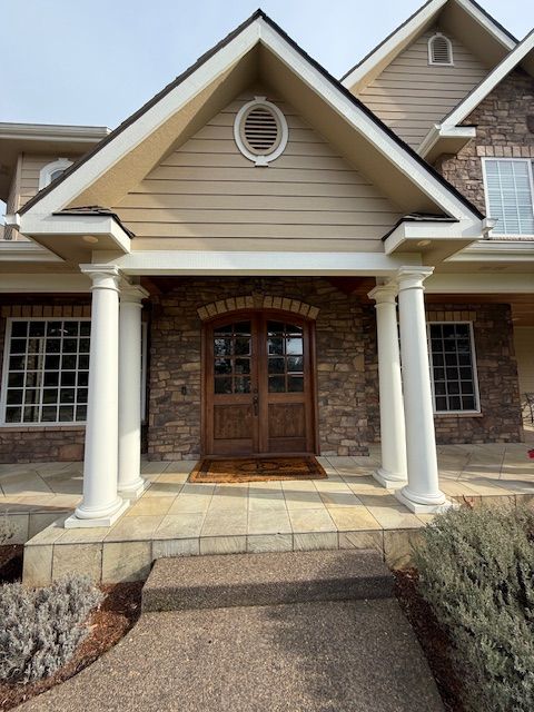 Front entrance of a beige house with a covered porch, white columns, and wooden double doors
