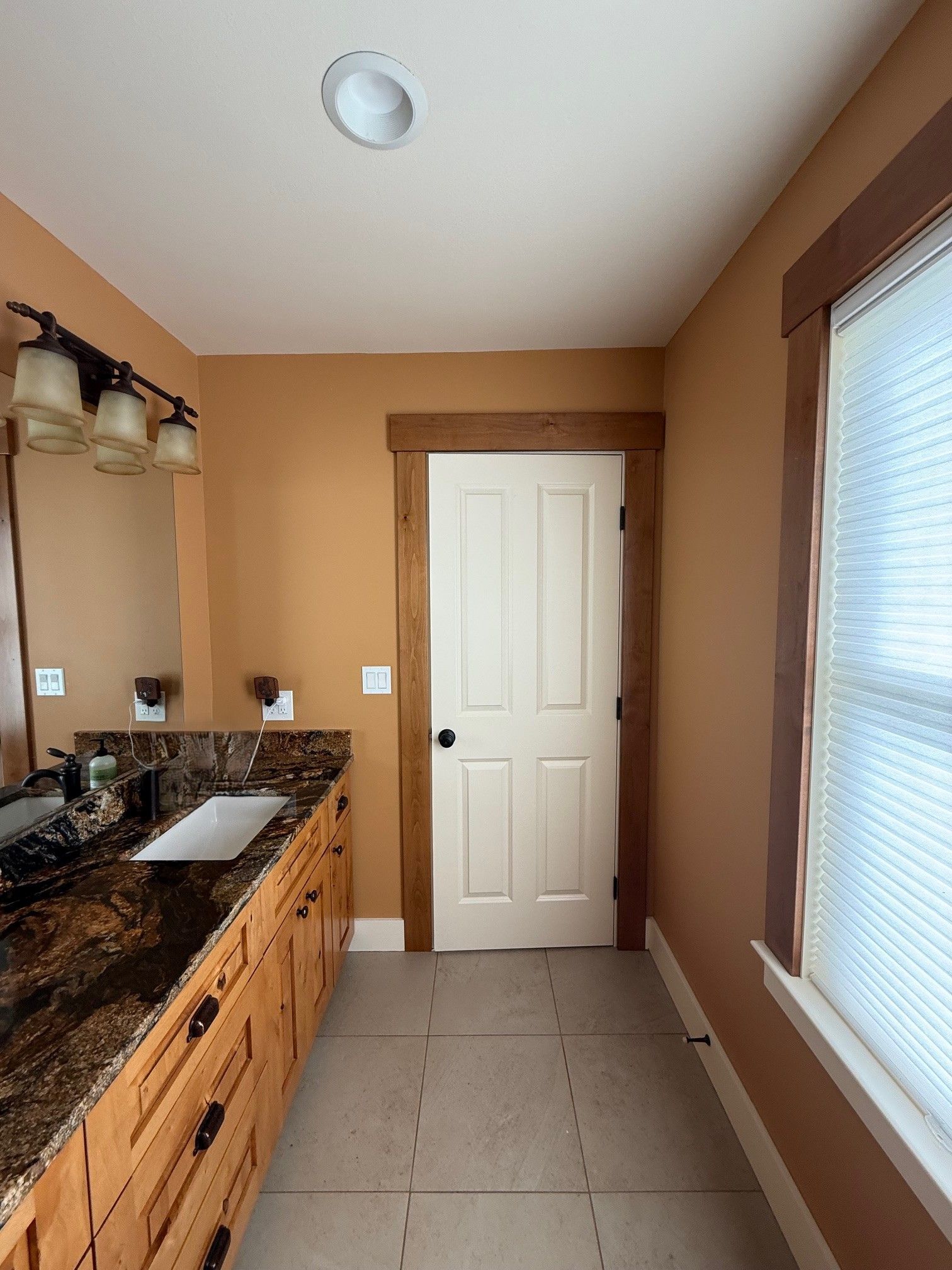 Bathroom with tan walls, white door, granite vanity, and tiled floor beside a frosted window.