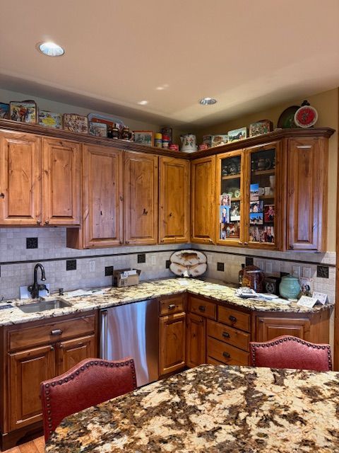 Wooden kitchen with granite countertops, tile backsplash, and a marble-patterned table in the foreground