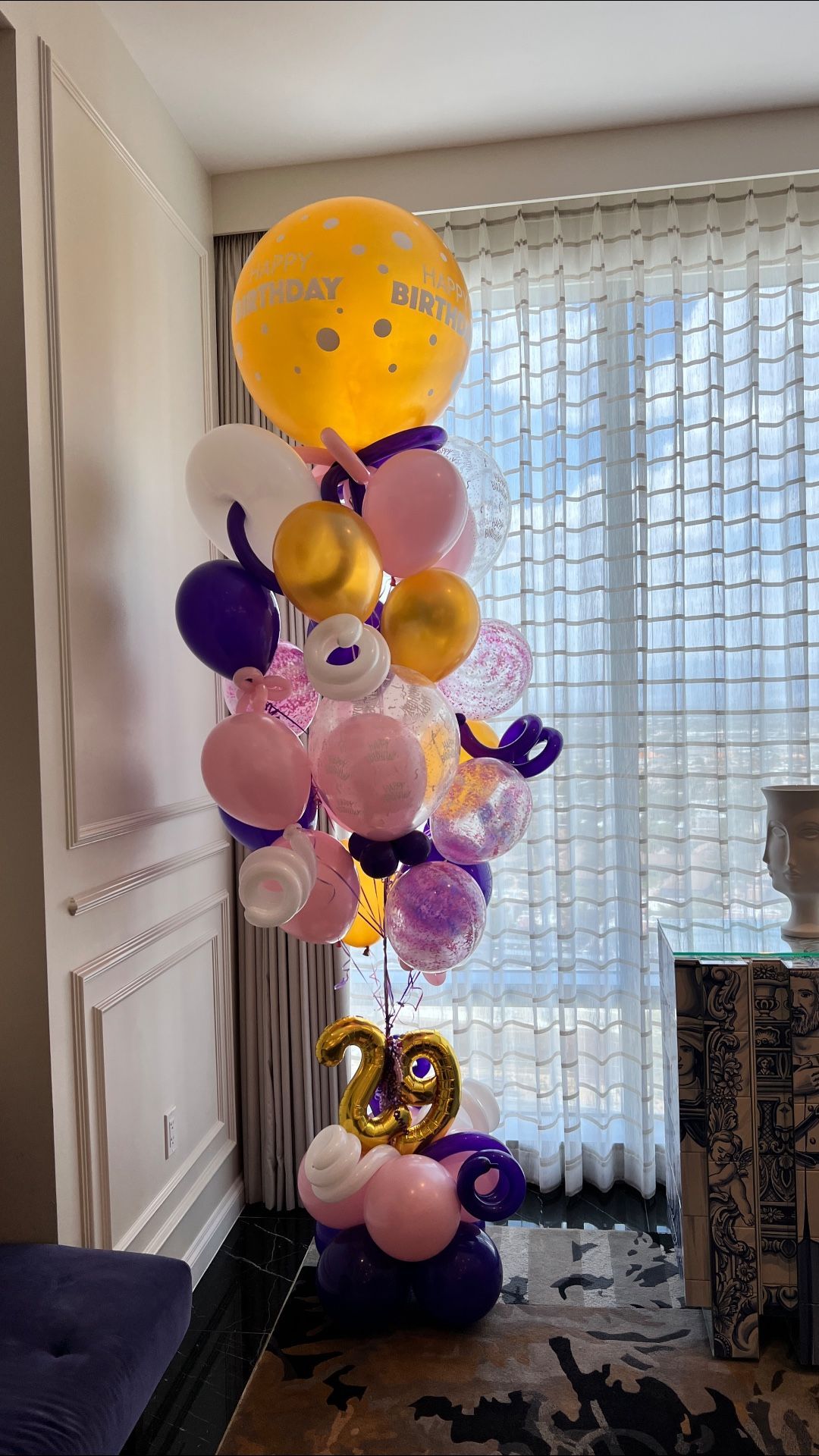 A bunch of balloons are sitting in a room next to a window.