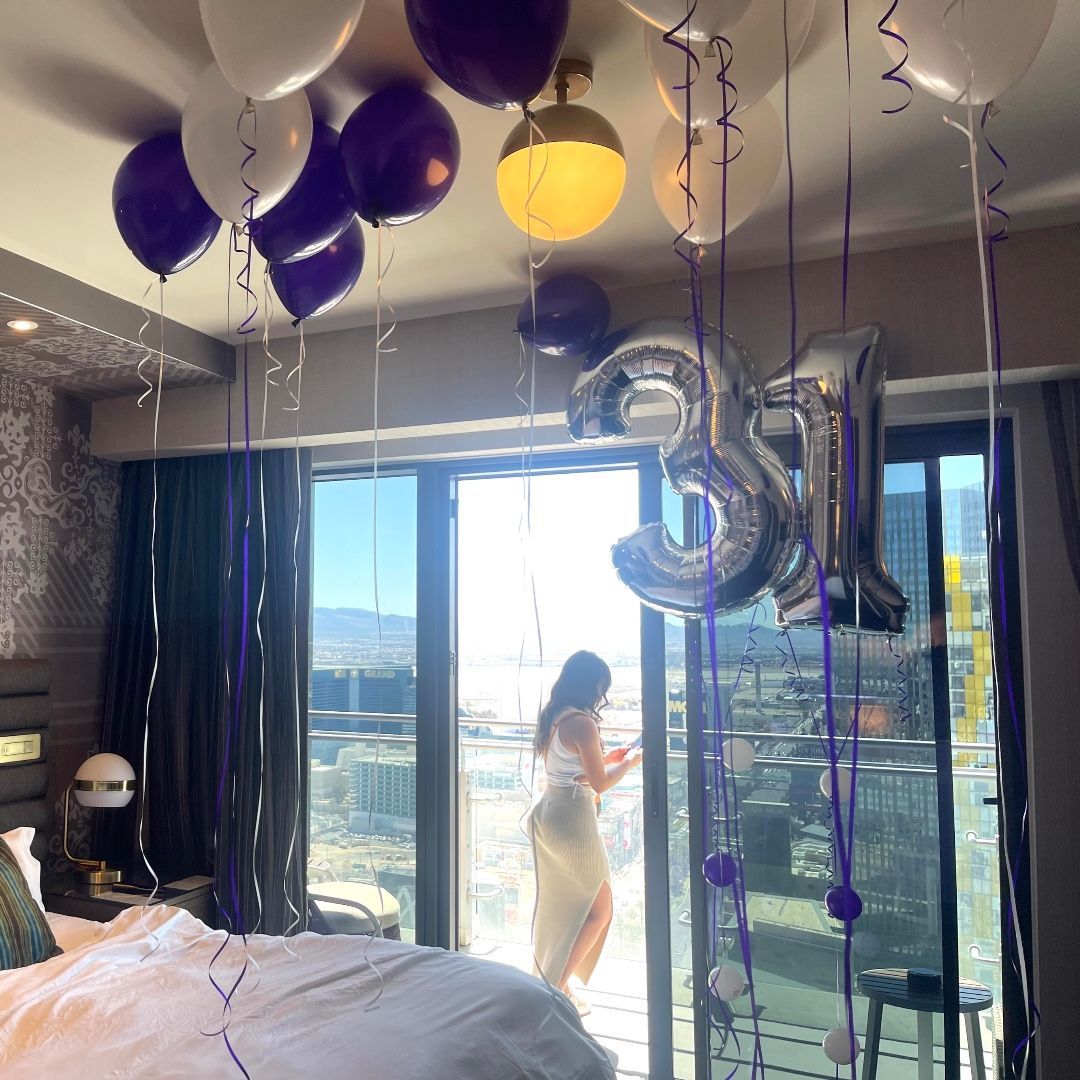 A woman is standing in a bedroom with balloons and a number 31