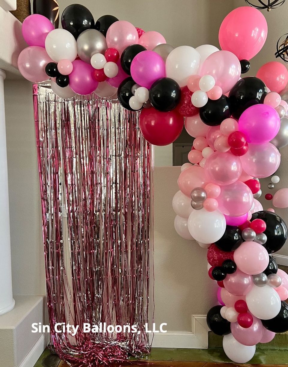 A bunch of pink and black balloons are sitting on a wall.