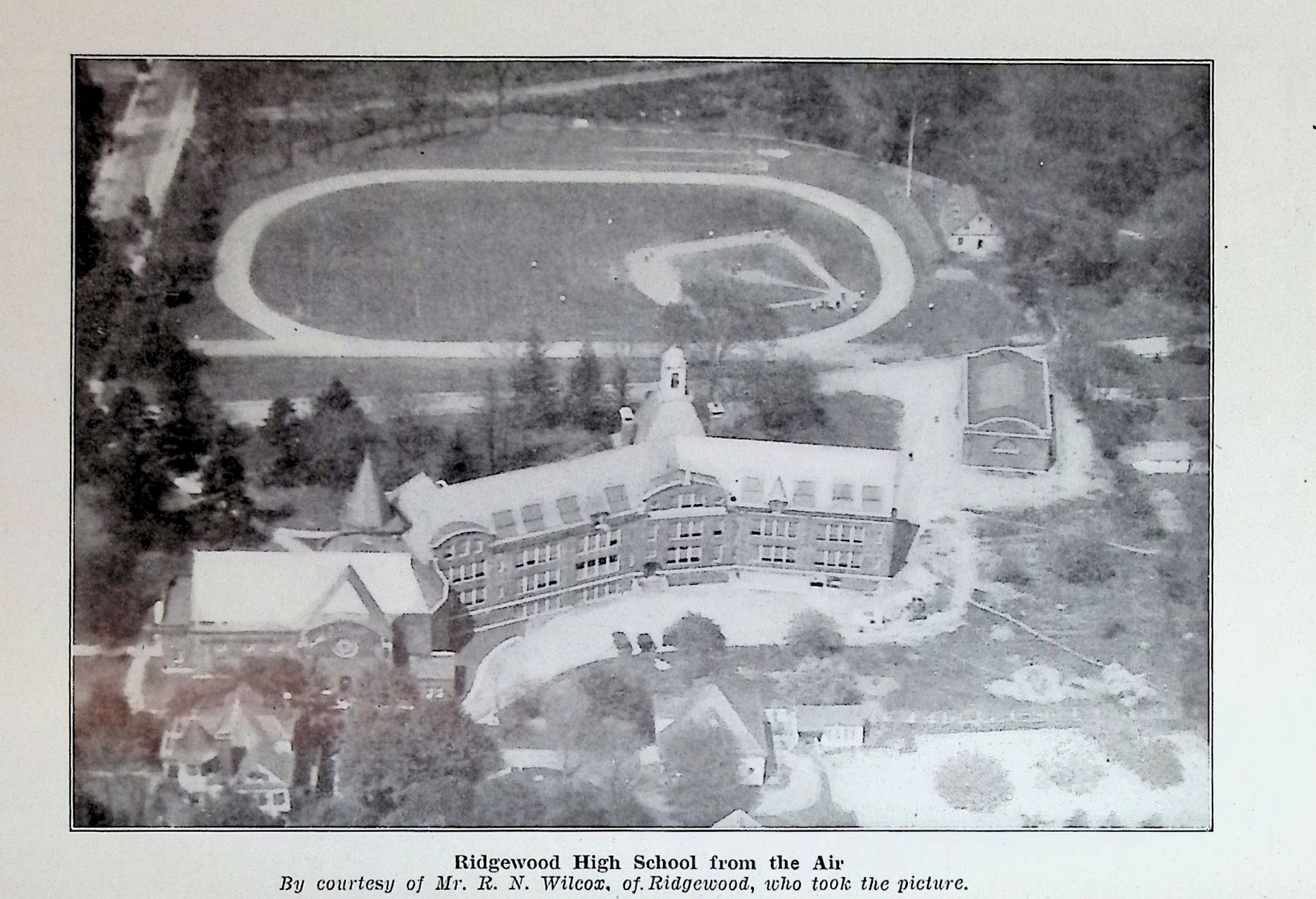 A black and white photo of a school with a baseball field in the background