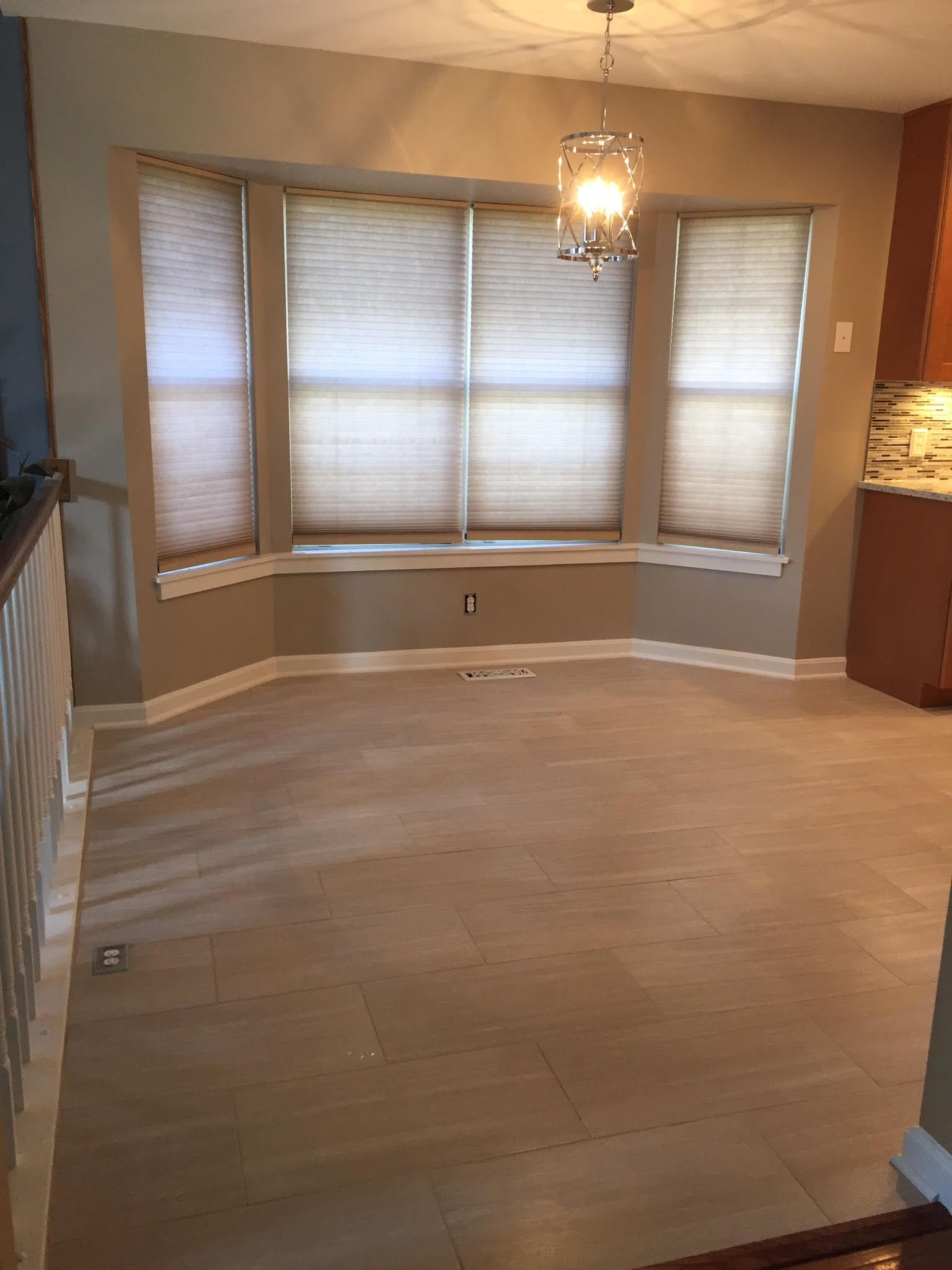 Empty dining area with large windows, tan floor, and a hanging light fixture.