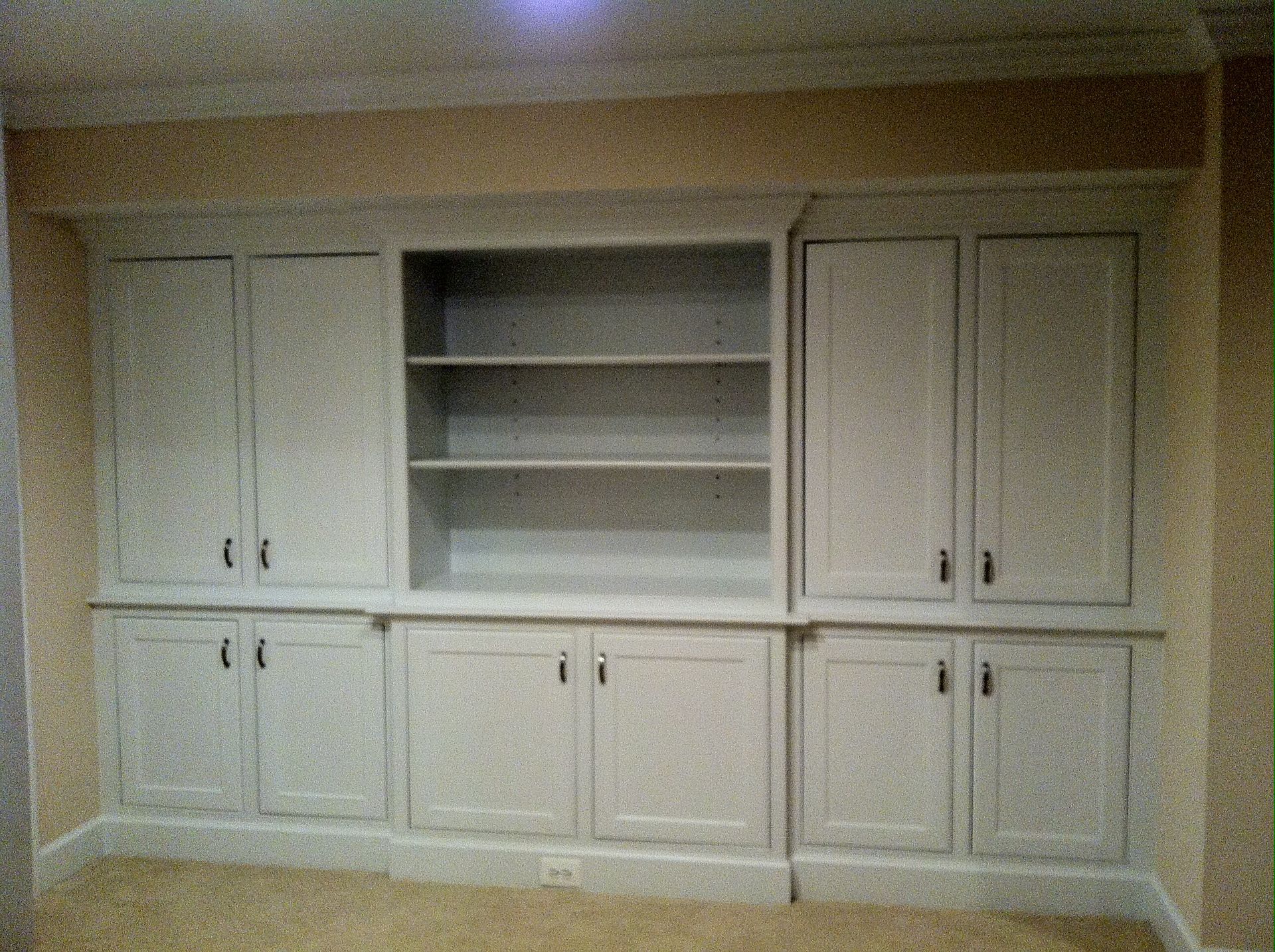 Built-in white cabinetry with upper cabinets, open shelving, and lower cabinets, set against a beige wall.
