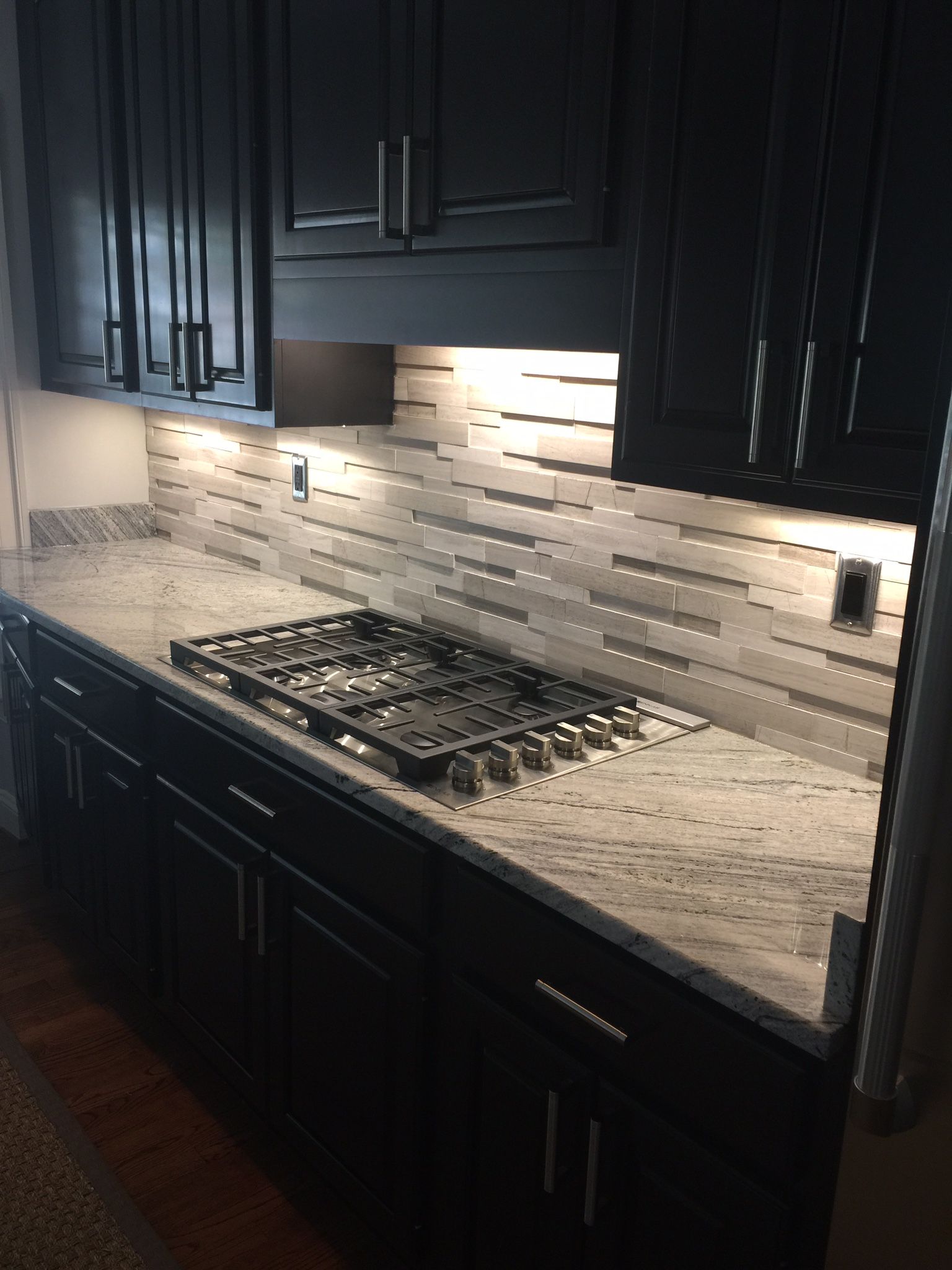 Black kitchen with granite countertop and tiled backsplash.
