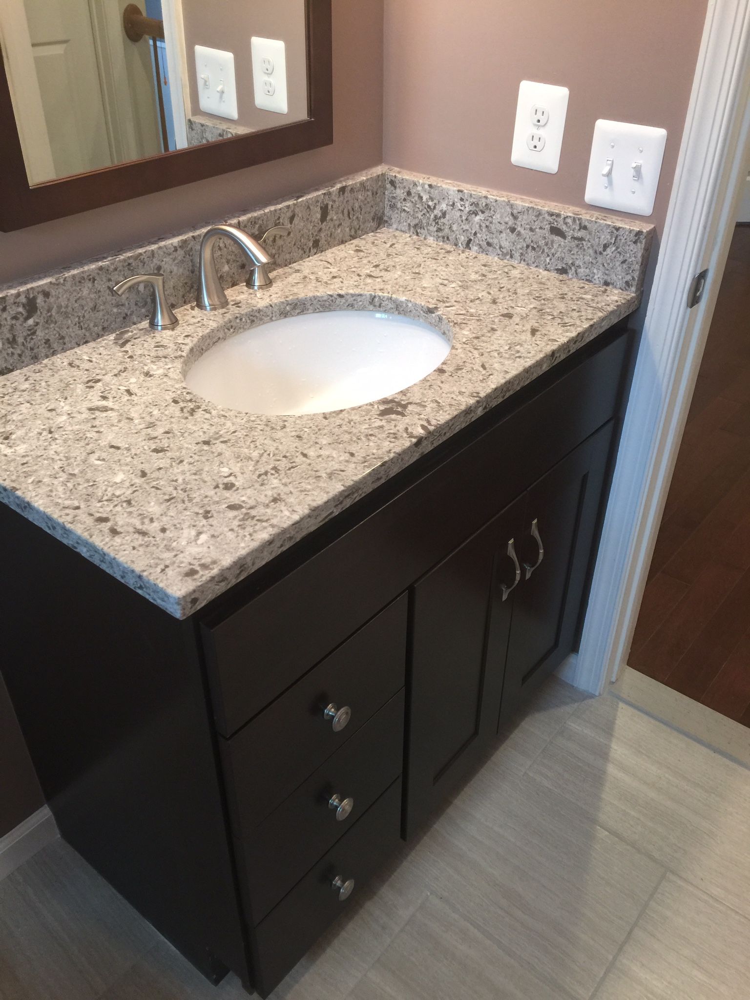 Dark brown bathroom vanity with granite countertop and oval sink.