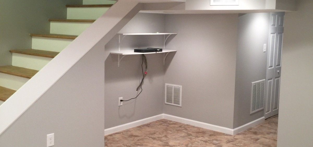 Under stairs storage area with shelves, a door, and vent. Gray walls, brown carpet.