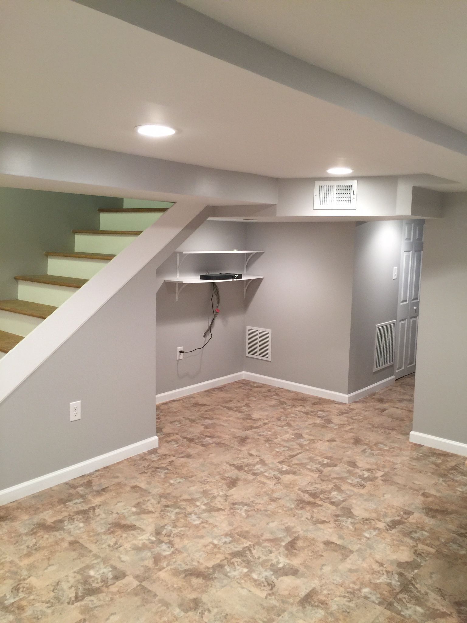 Finished basement interior with stairs, neutral paint, built-in shelves, and patterned flooring.
