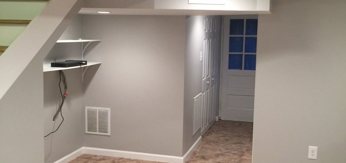 Interior view of a newly painted basement. Shelves, an access door, and ventilation vents are visible.