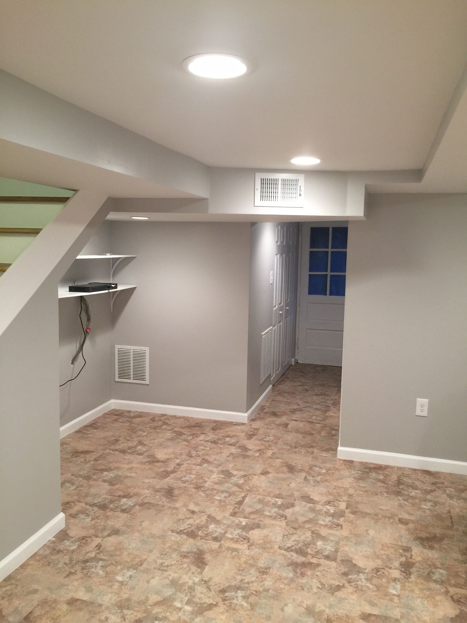 A finished basement with gray walls, recessed lighting, and a doorway leading to a white door.