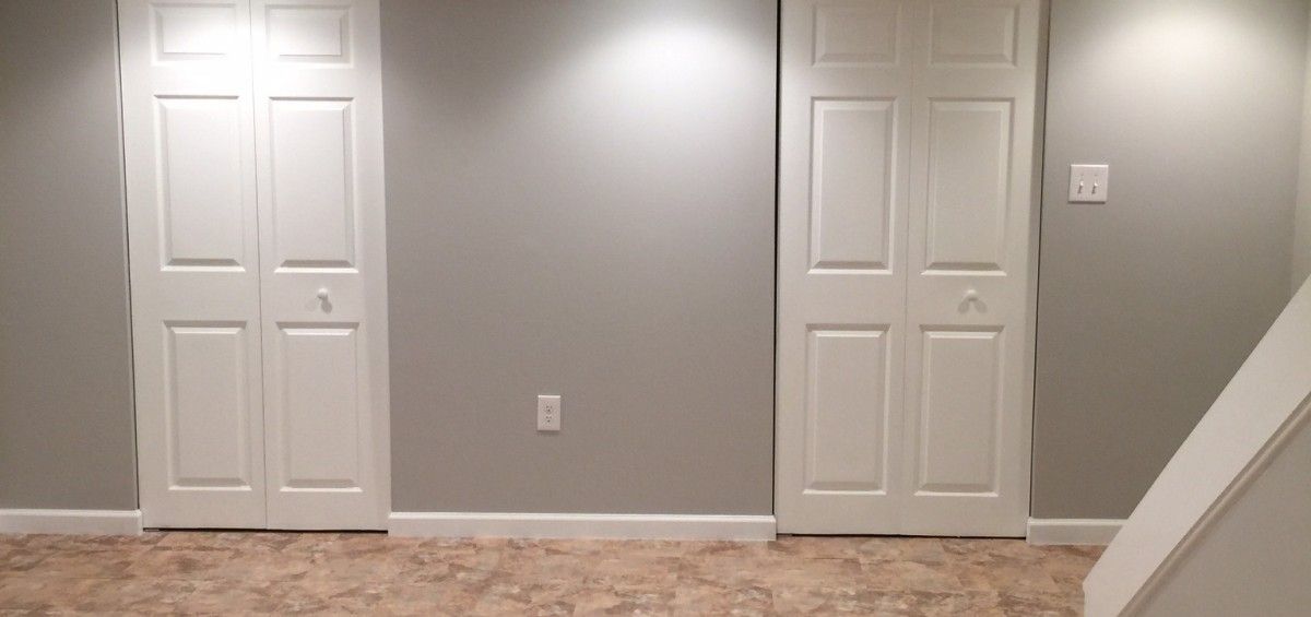 A room with two white closet doors and gray walls, a brown carpet, and a staircase.
