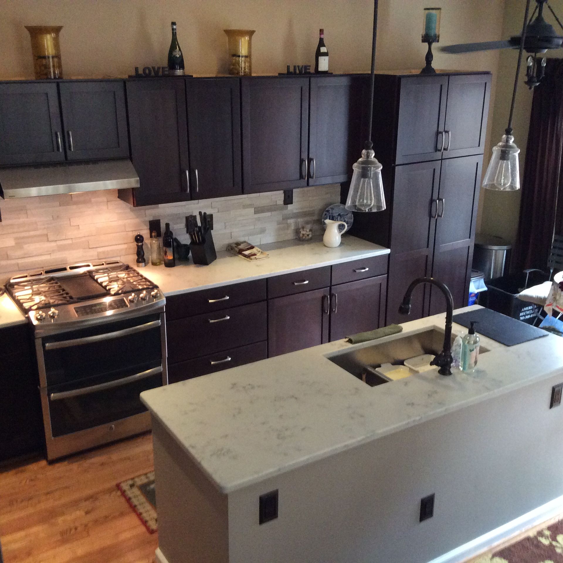 Dark-cabinet kitchen with white countertops and island, stainless steel appliances.