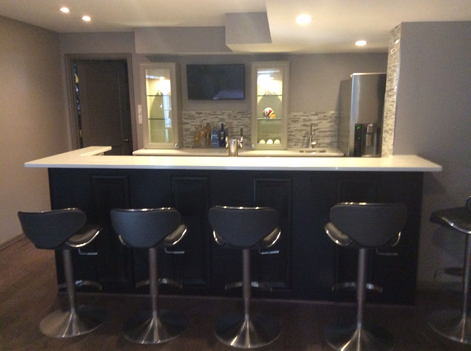 A home bar with black cabinets, white countertop, and gray stools.