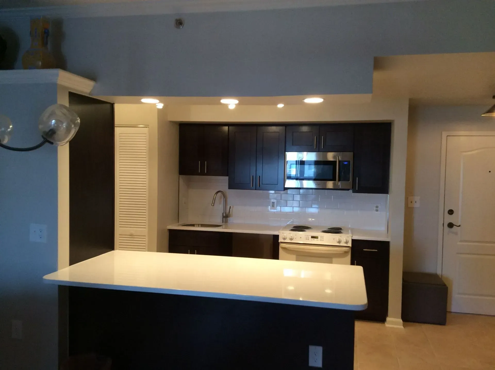 Modern kitchen with dark cabinets, white countertop island, and stainless steel appliances.