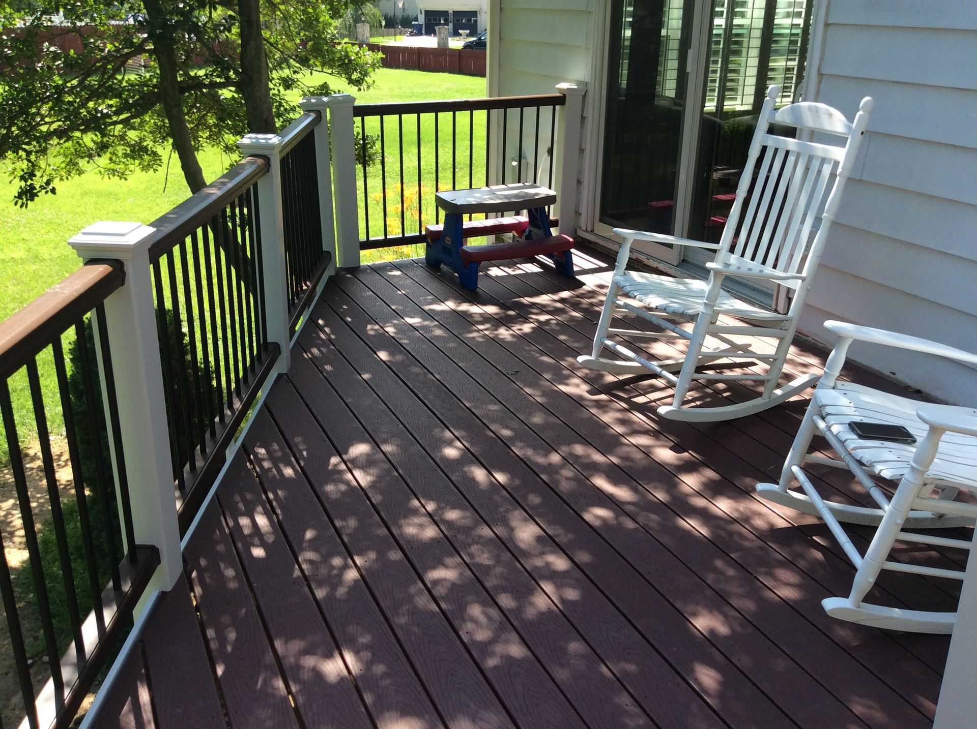 Deck with brown boards, white railing posts, and two rocking chairs.