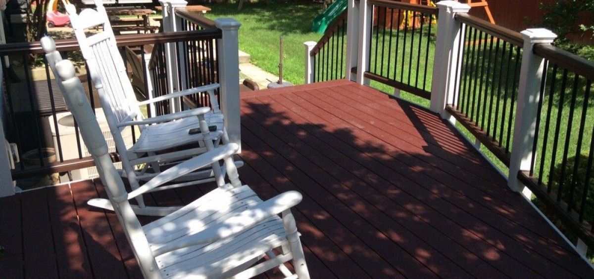White rocking chair on a wooden deck overlooking a yard with a playground.