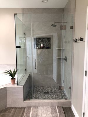 Modern, glass-enclosed shower with pebble floor, built-in shelves, and a bench.