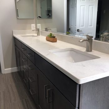 Bathroom with dark vanity, white countertop, two sinks, mirrors, and brushed nickel faucets.