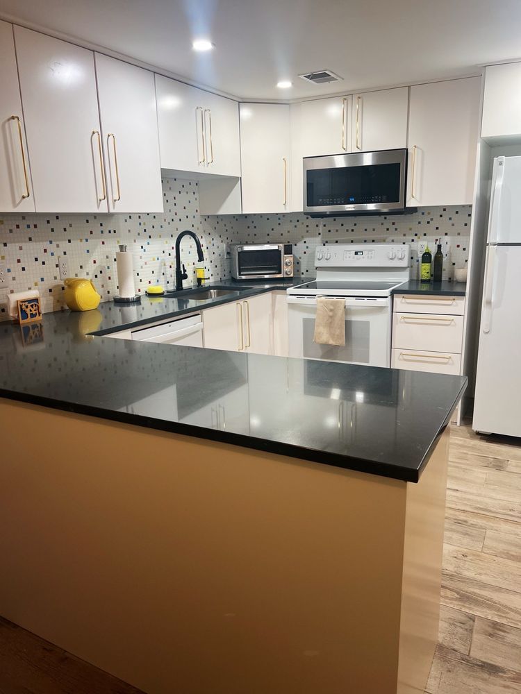 Modern kitchen with white cabinets, black countertops, and stainless steel appliances.