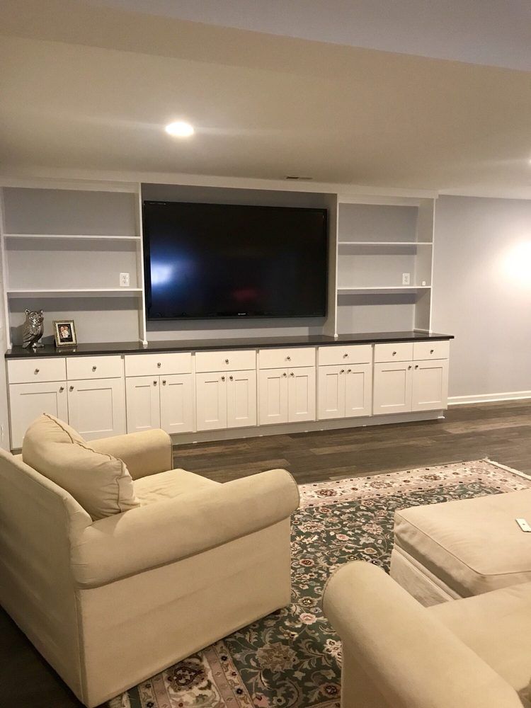Living room with built-in entertainment center, white cabinets, TV, and cream-colored sofa.
