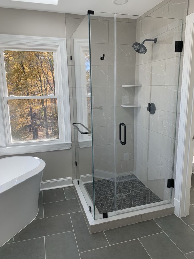 Modern bathroom with glass shower, gray tiles, and white soaking tub.