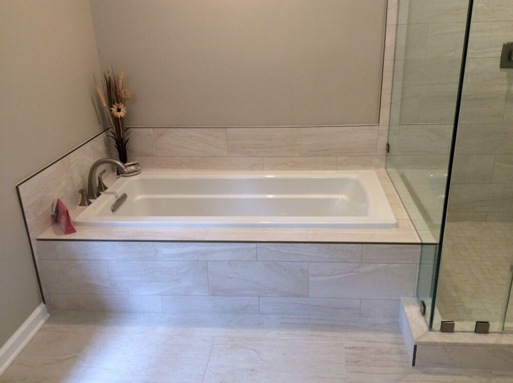 A built-in white bathtub surrounded by light tile in a modern bathroom.