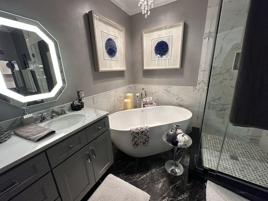 Luxurious bathroom with gray vanity, oval tub, and marble shower. Blue and white artwork on gray walls.