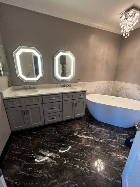 Gray bathroom with double vanity, oval tub, and dark marble floor.