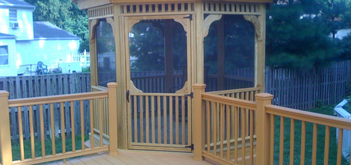 Wooden gazebo on a deck with railings, set in a backyard.