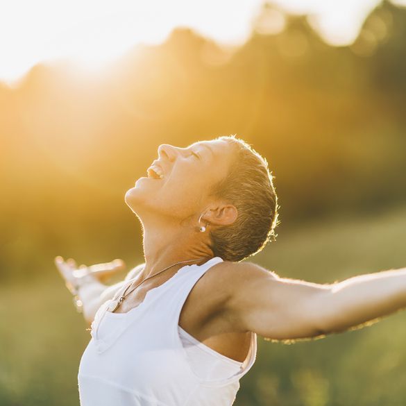 Person with arms outstretched, smiling in warm sunlight outdoors.