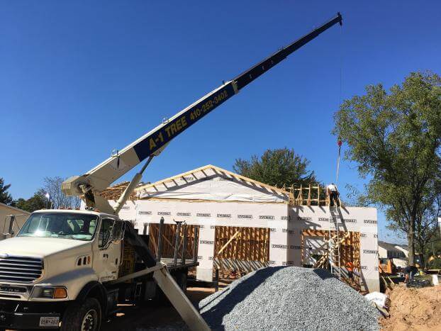 A truck with a crane attached to it is parked in front of a house under construction