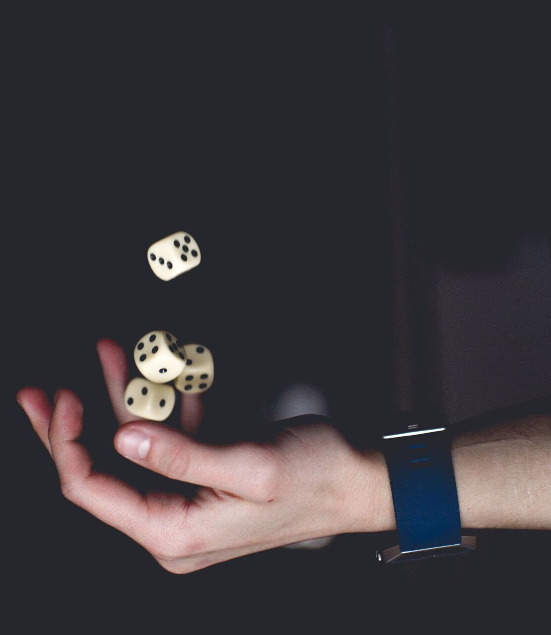 Hand catching three dice in midair against a dark background, wearing a blue wristband.