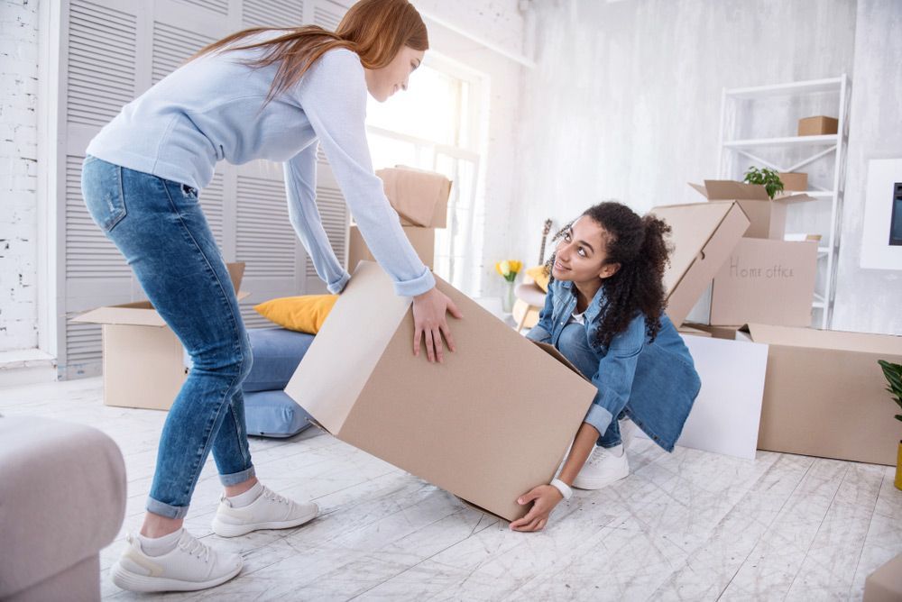 Two Women Are Carrying Boxes in a Living Room — Davis Removals & Storage in Adelaide, SA
