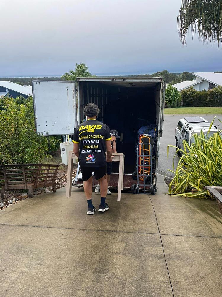 A Man is Carrying a Table Into a Truck — Davis Removals & Storage in Dundowran, QLD