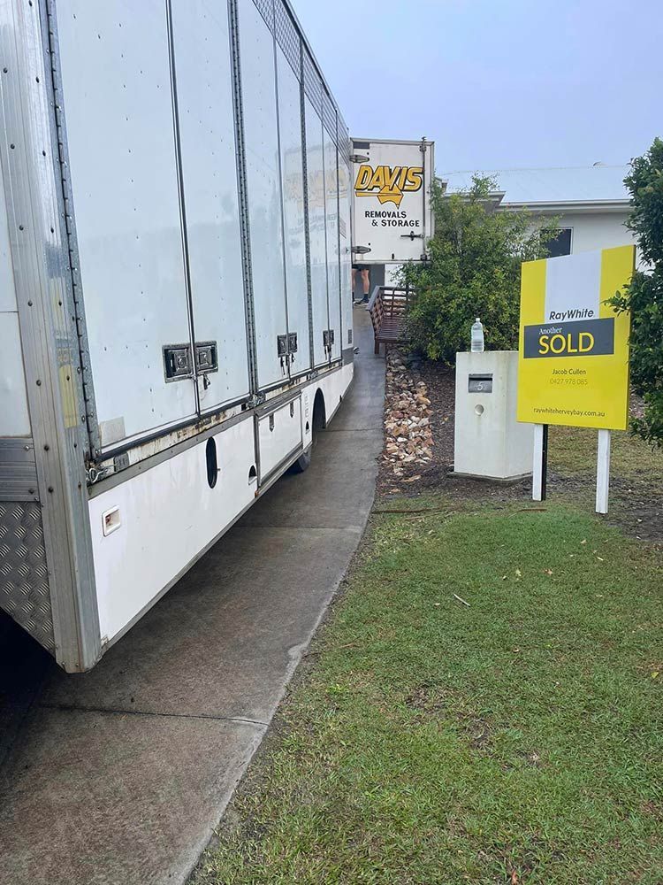 A White Trailer is Parked on the Side of the Road Next to a Sold Sign — Davis Removals & Storage in Maryborough, QLD