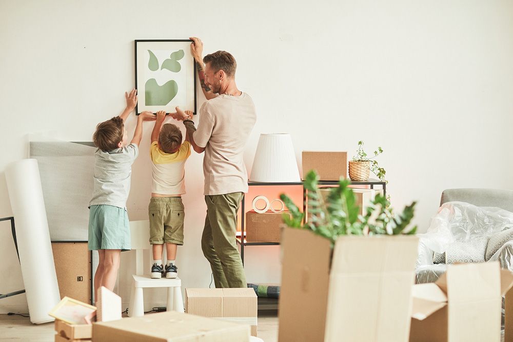 A Man and Two Children Are Hanging a Picture on a Wall in a Living Room — Davis Removals & Storage in Newcastle, NSW