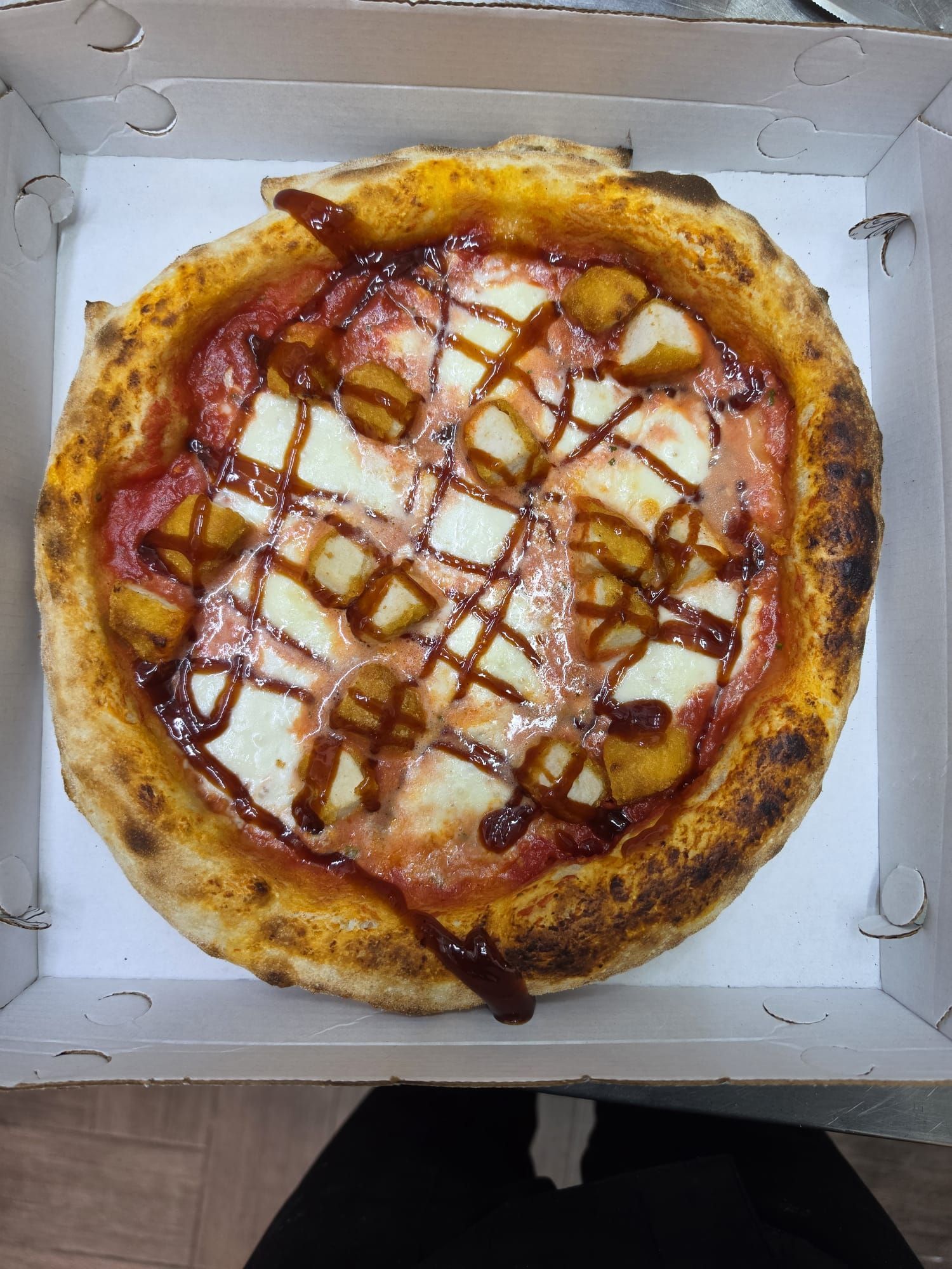 Pizza con formaggio fuso e glassa rossa in una scatola bianca da asporto, vista dall'alto.