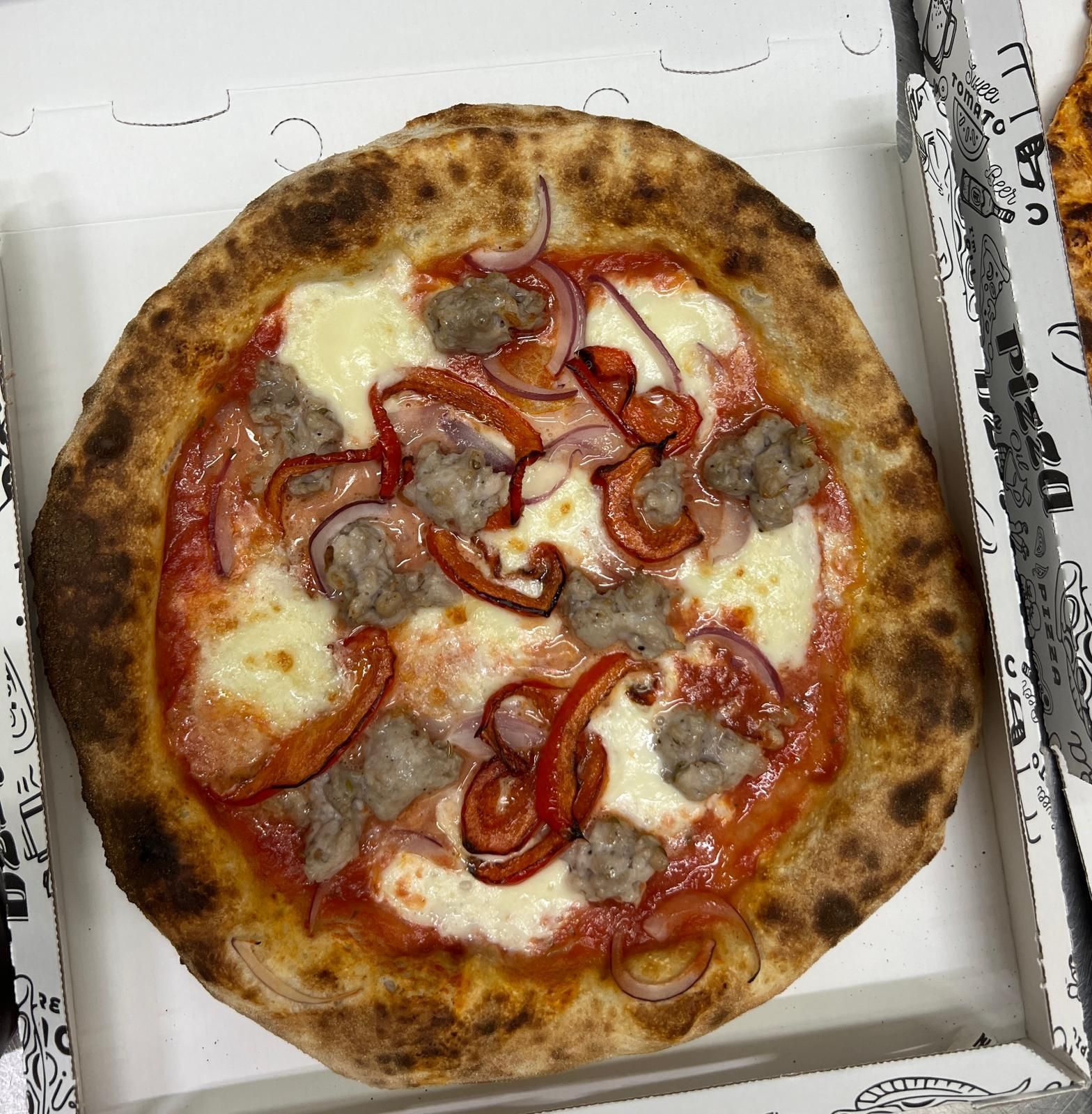 Pizza in scatola con salsiccia, cipolla rossa e fette di peperone rosso su formaggio fuso