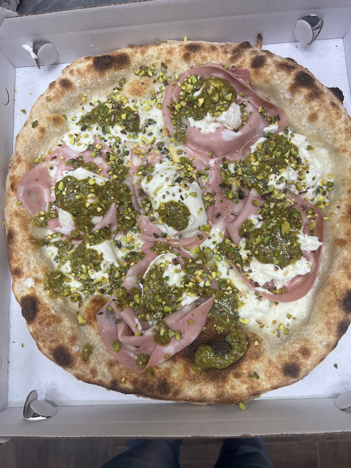 Pizza con cipolle rosse, pesto verde e formaggio fuso in una scatola di cartone aperta.