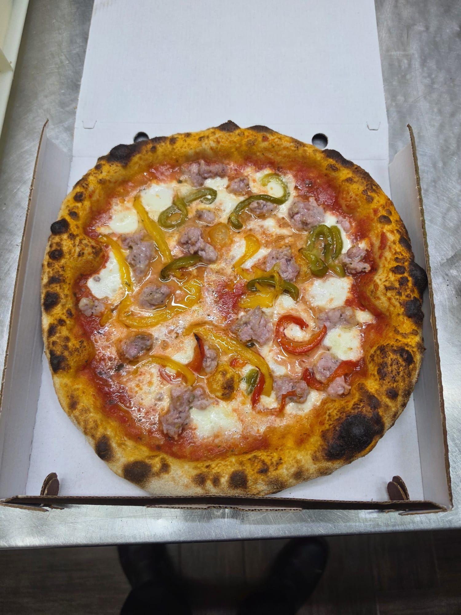 Pizza in una scatola aperta, condita con formaggio, peperoni e salsiccia, con una crosta bruciacchiata.