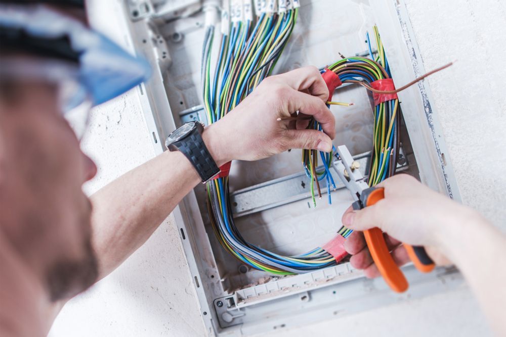 Electrician Working on Wiring Inside a Wall-mounted Electrical Panel — Gold City Solar & Electrical in Hervey Bay, QLD