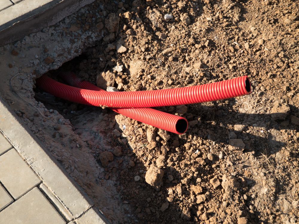 Red Corrugated Tubes Emerge from a Hole in Concrete — Gold City Solar & Electrical in Maryborough, QLD