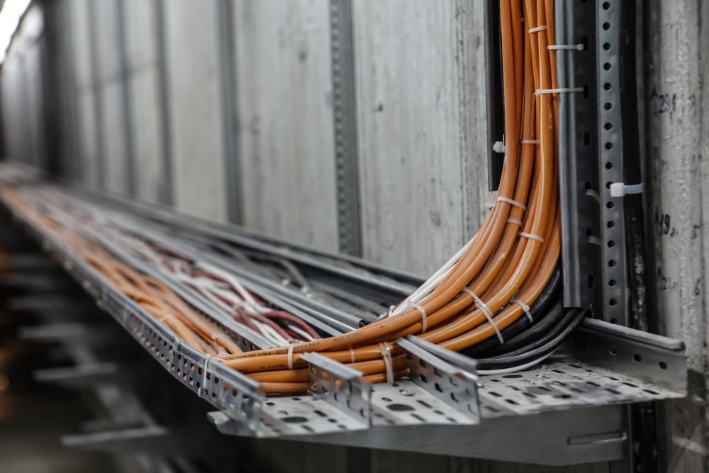 Cable Tray with Orange and Black Wires Secured Against a Gray Concrete Wall — Gold City Solar & Electrical in Hervey Bay, QLD