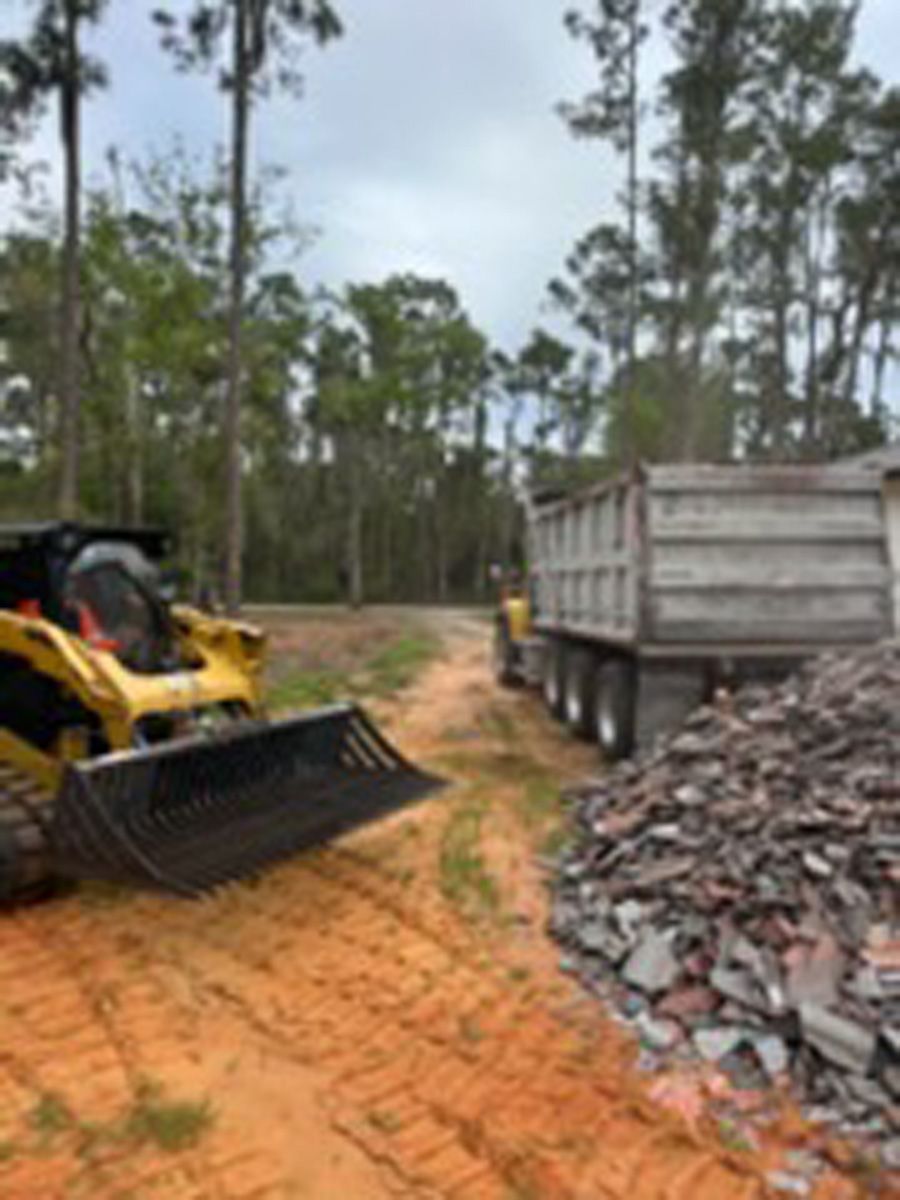 Yellow bulldozer beside a truck and pile of rubble on a dirt road in a wooded area
